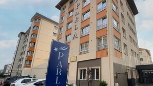 Ein mehrgeschossiges Hotel namens PARLA mit modernem Design, das einen markanten Eingang und einen Parkbereich mit mehreren Autos bietet.