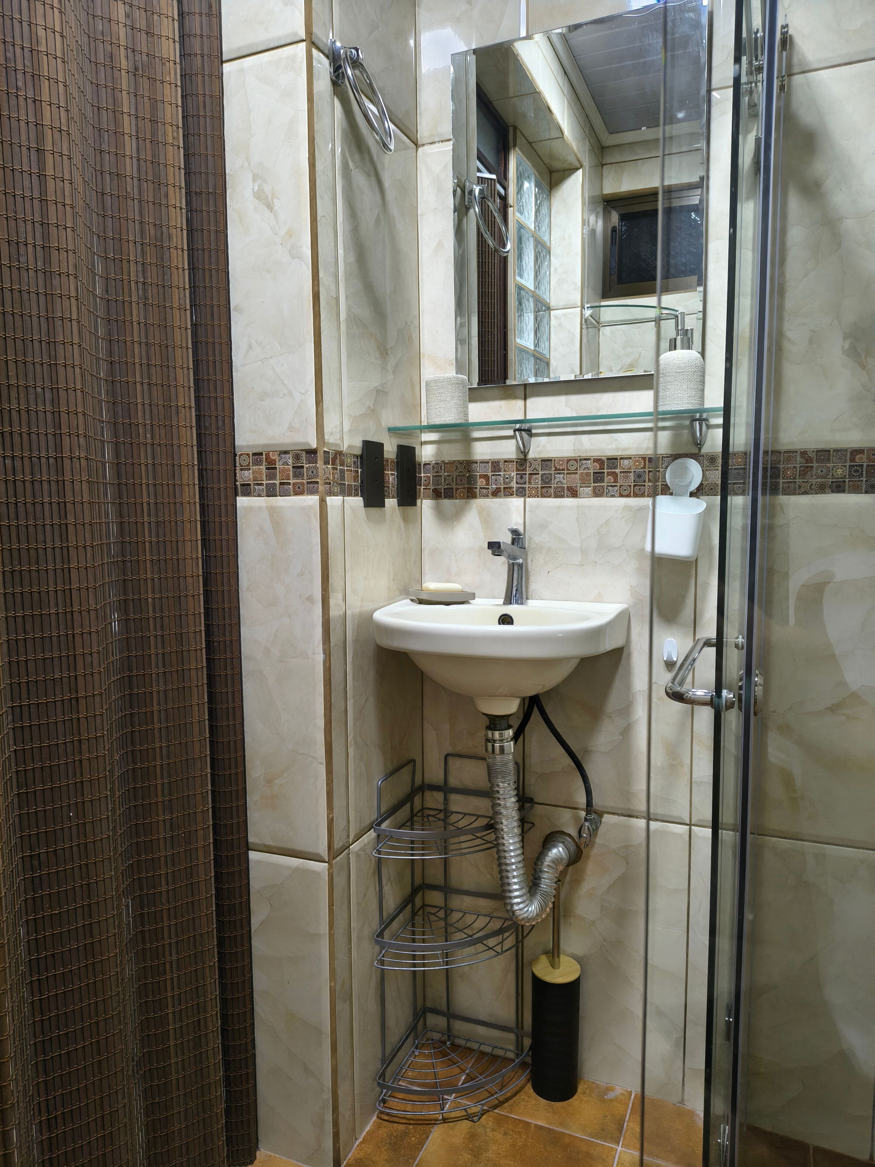 A bathroom with a glass shower enclosure, a sink with a glass shelf above, and a toilet with a paper towel holder.