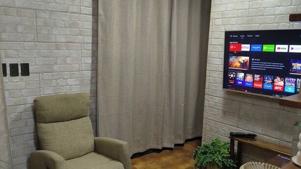 Ein Wohnzimmer mit beigefarbenem Sessel, einem Flachbildfernseher, der an einer Ziegelwand angebracht ist, und einem Deckenventilator.