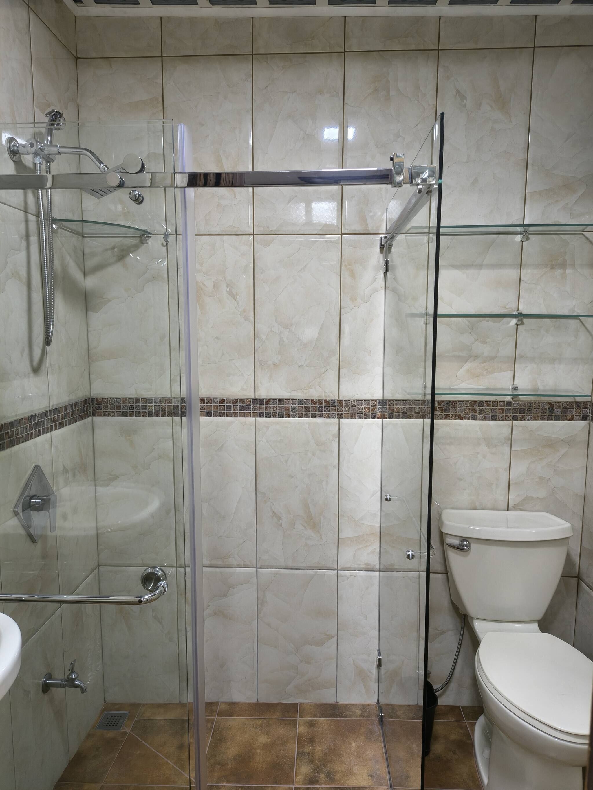 A bathroom with a glass-enclosed shower, a white toilet, and a sink with a chrome faucet.