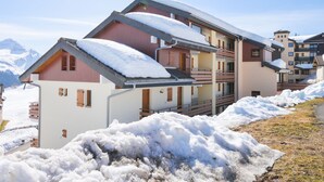 A multi-story hotel with snow-covered roofs, a balcony, and a mountain backdrop.