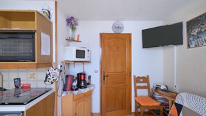 A compact kitchen with a microwave, oven, and coffee maker, a wooden door, and a TV mounted on the wall.