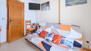 A bedroom with a bed, a wooden door, a television, and a painting on the wall.