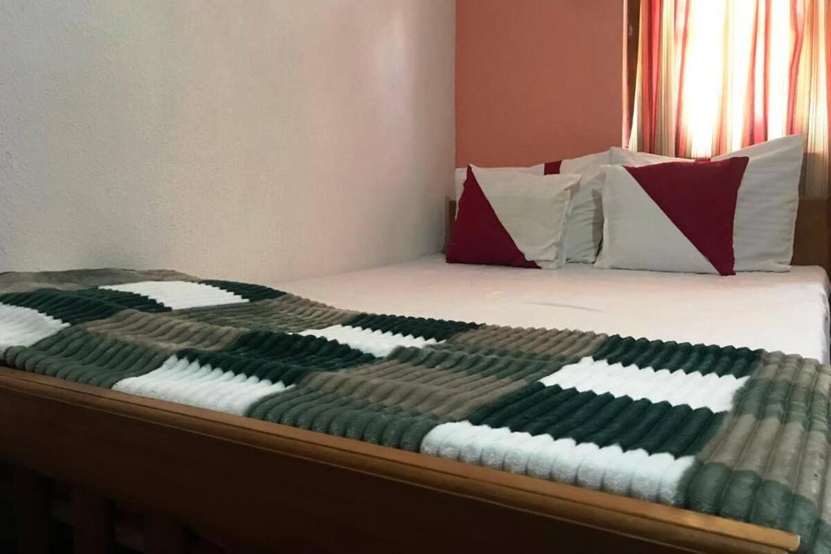 Una cama bien hecha con un edredón de cuadros, un cabecero de madera y una pared con una única ventana.