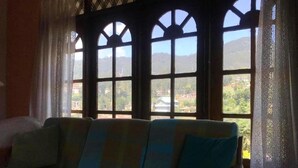 A room with a sofa facing large windows with a view of a mountainous landscape. - Aurora Residence Nuwara (Nuwara Eliya)