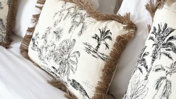 Ein Bett mit weißer Bettwäsche und Kissen mit schwarzen Blättermustern im tropischen Stil.