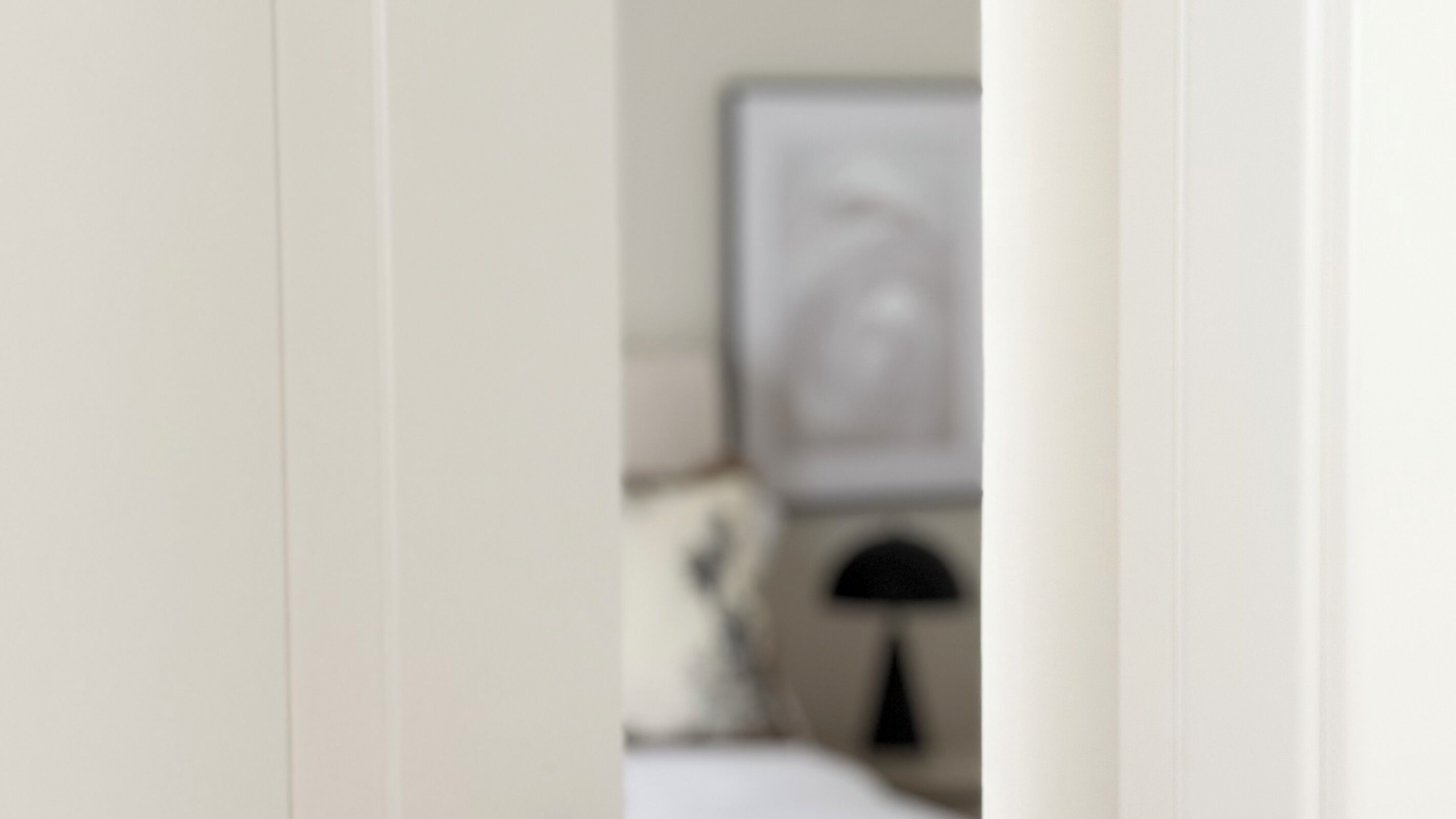 Vista borrosa del interior de una habitación de hotel con una cama, una mesita de noche y una lámpara fijada a la pared.