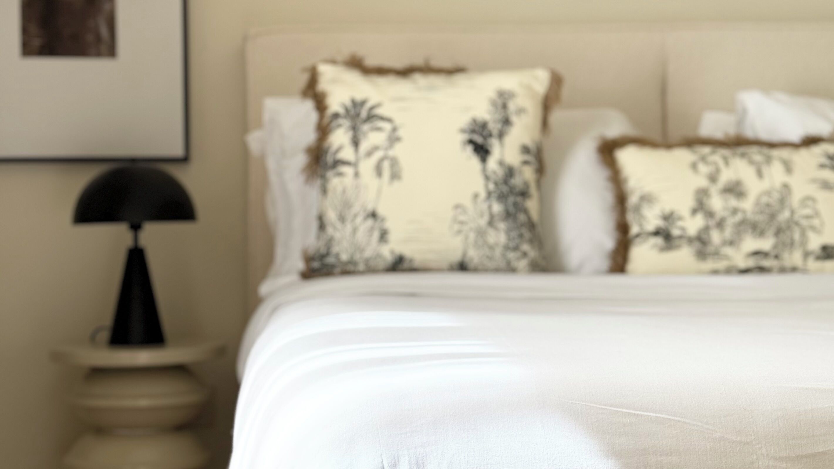 Un lit avec une literie blanche et deux coussins décoratifs ornés de motifs floraux.