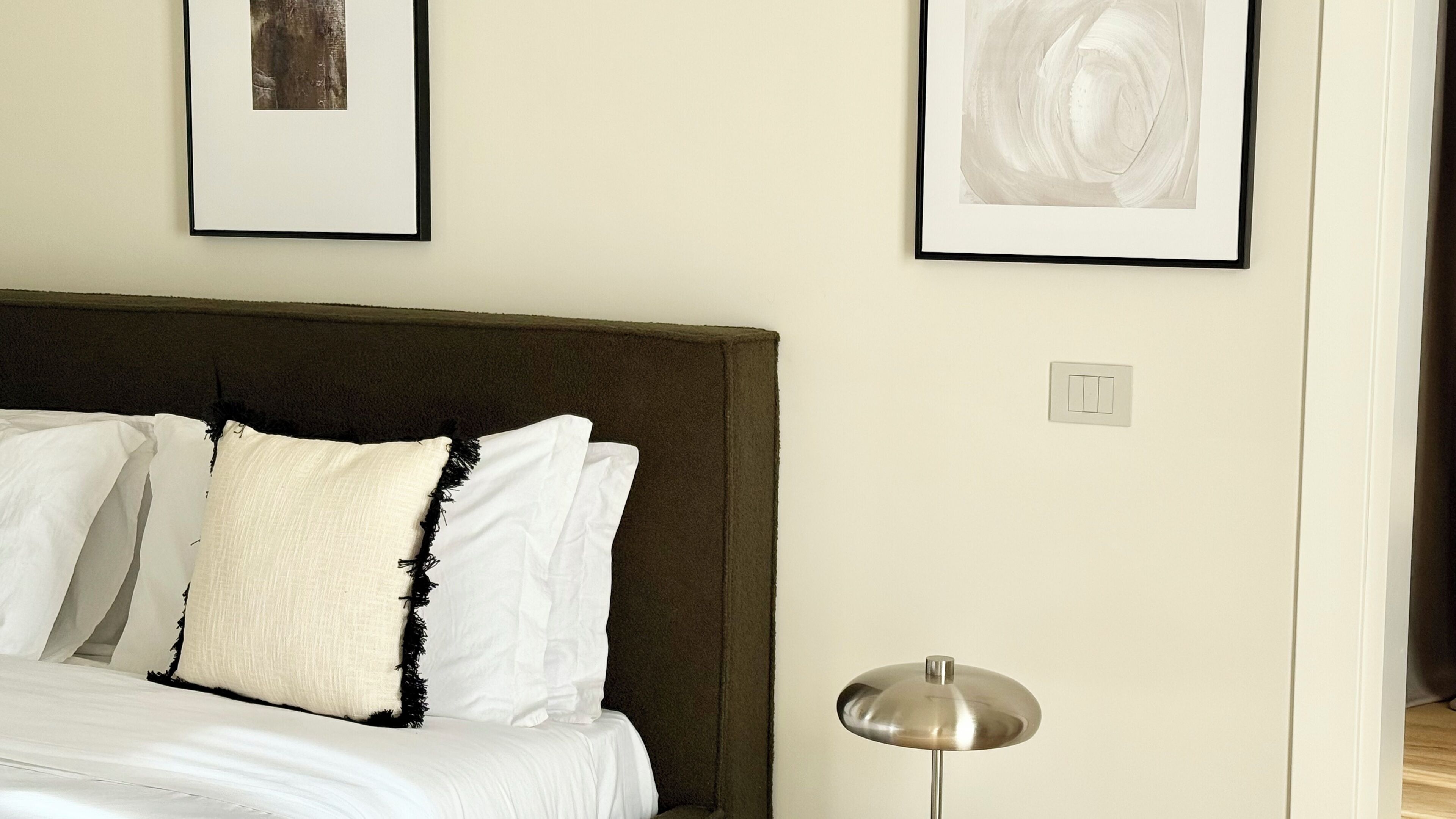 Un dormitorio con una cama, almohadas blancas, un cabecero oscuro y dos obras de arte abstractas enmarcadas en la pared.