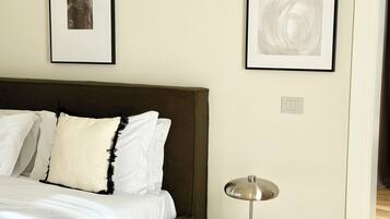 Un dormitorio con una cama, almohadas blancas, un cabecero oscuro y dos obras de arte abstractas enmarcadas en la pared.