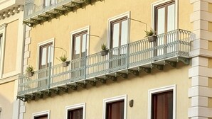 Ένα κτίριο με πολλά παράθυρα και μπαλκόνια, μερικά από τα οποία διακοσμούνται με φυτά σε γλάστρες.