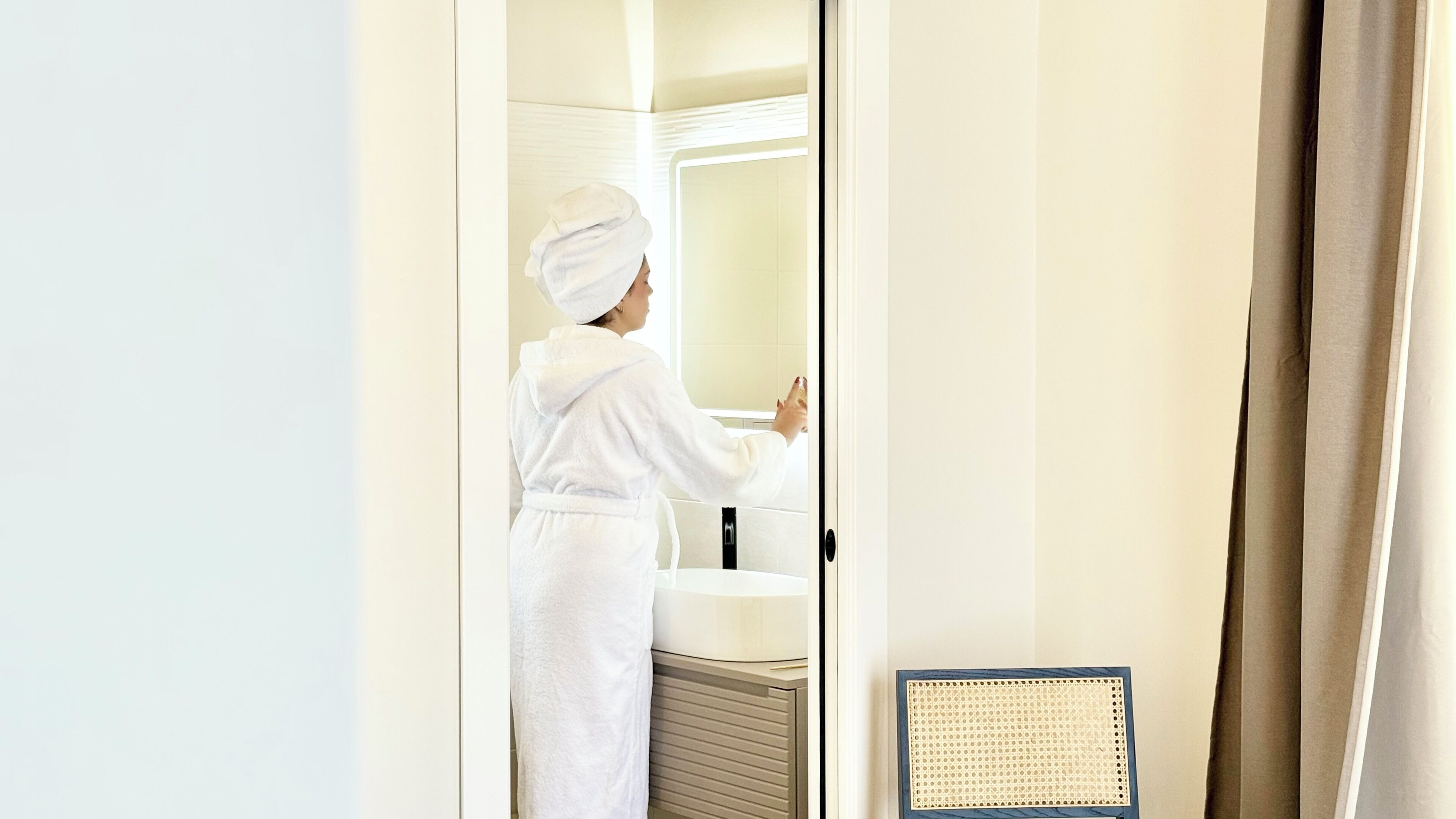 A person in a white robe standing in a bathroom with a sink and a mirror.