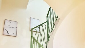 Μια σκάλα με πράσινο κάγκελο και δύο έργα τέχνης σε κορνίζες τοποθετημένα στον τοίχο.