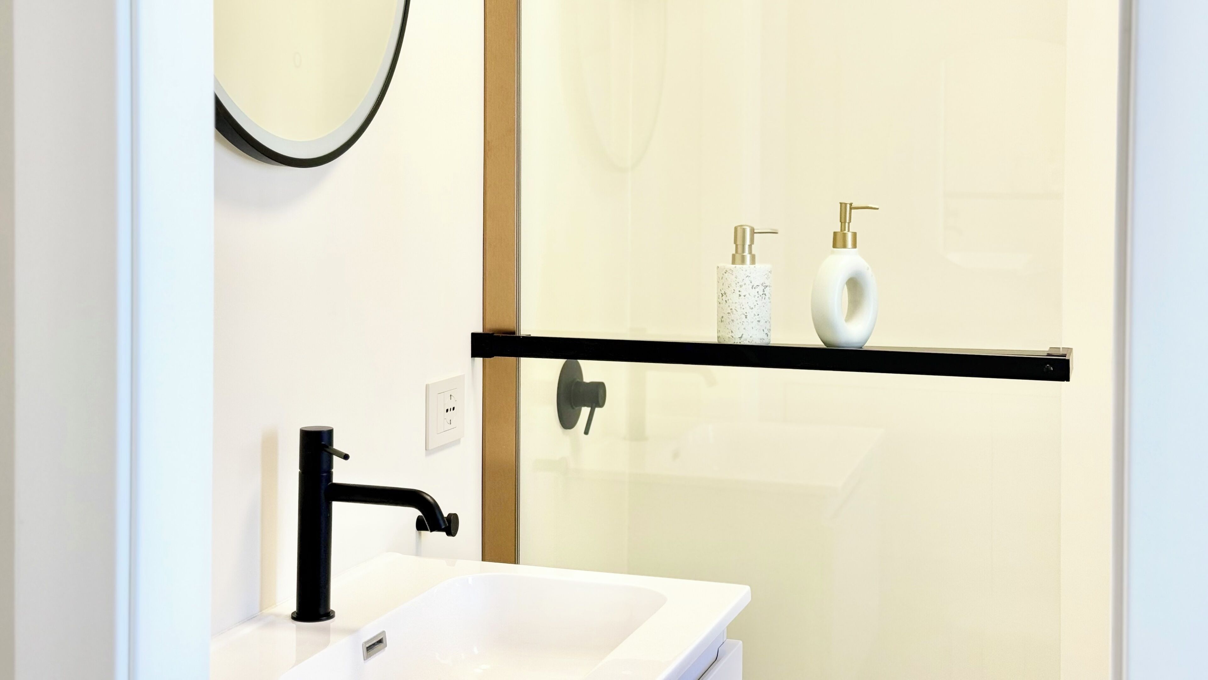 Un baño con lavamanos blanco, grifo negro y cabina de ducha de vidrio.
