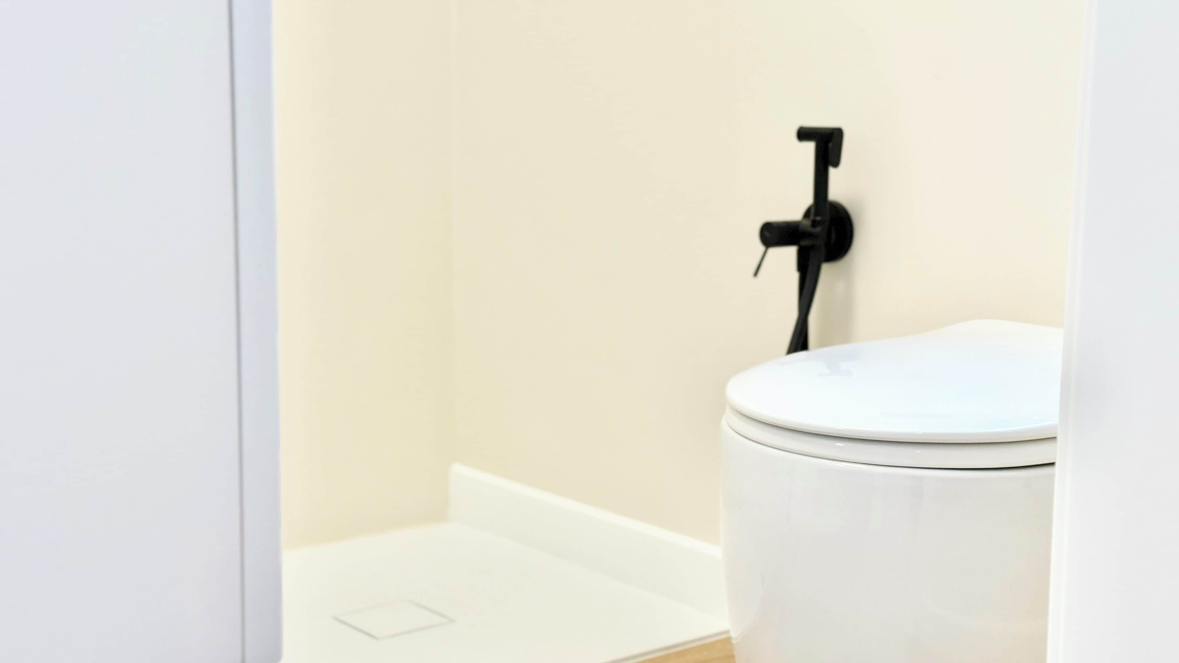 A bathroom with a white toilet, a shower area, and a wall-mounted faucet.