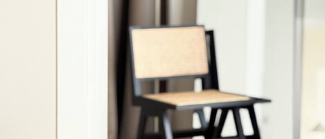 A chair with a woven backrest and seat, positioned in a room with a plain wall and a door in the background.
