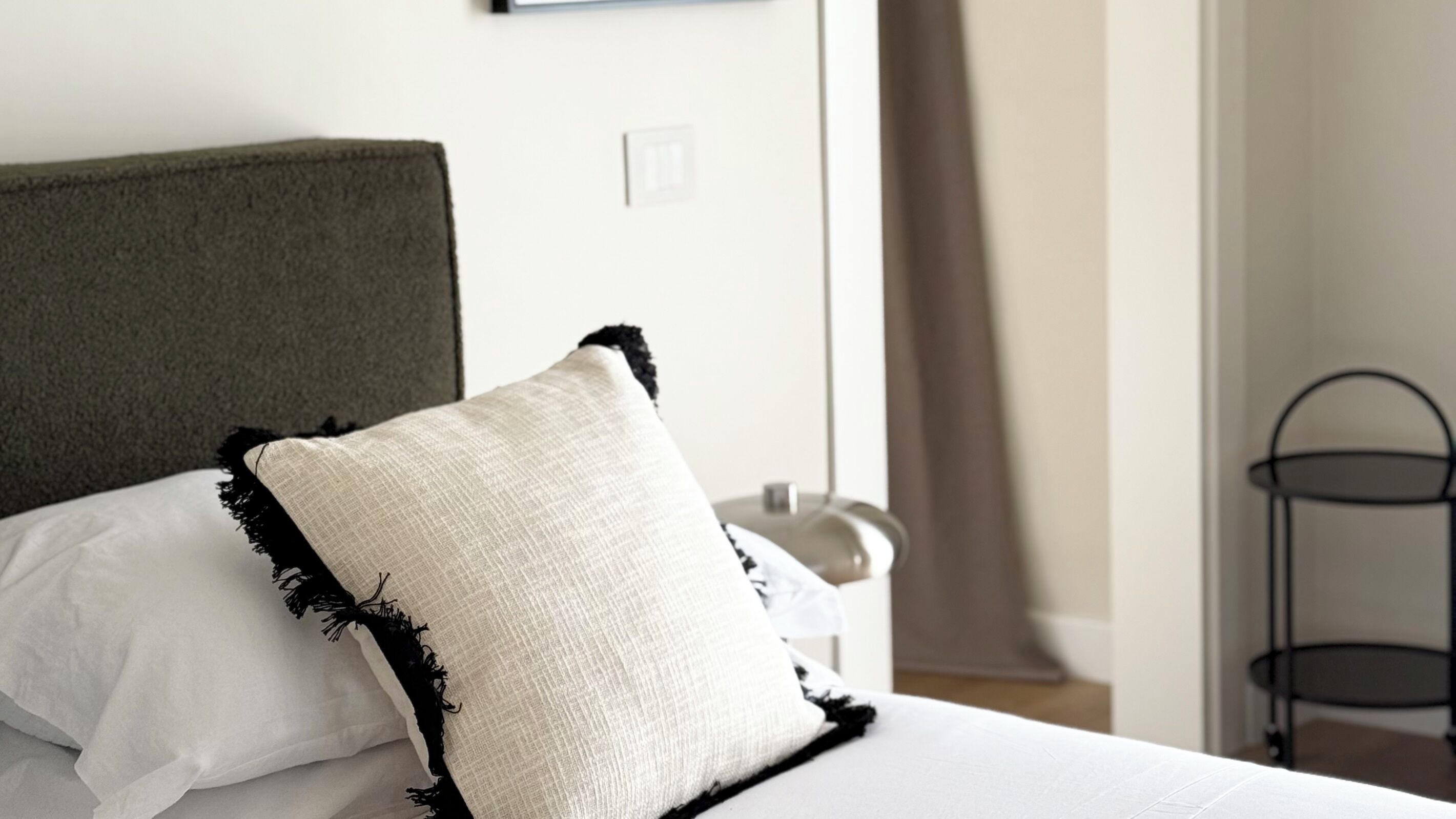 A bed with a green headboard, white bedding, and a white pillow with black trim.