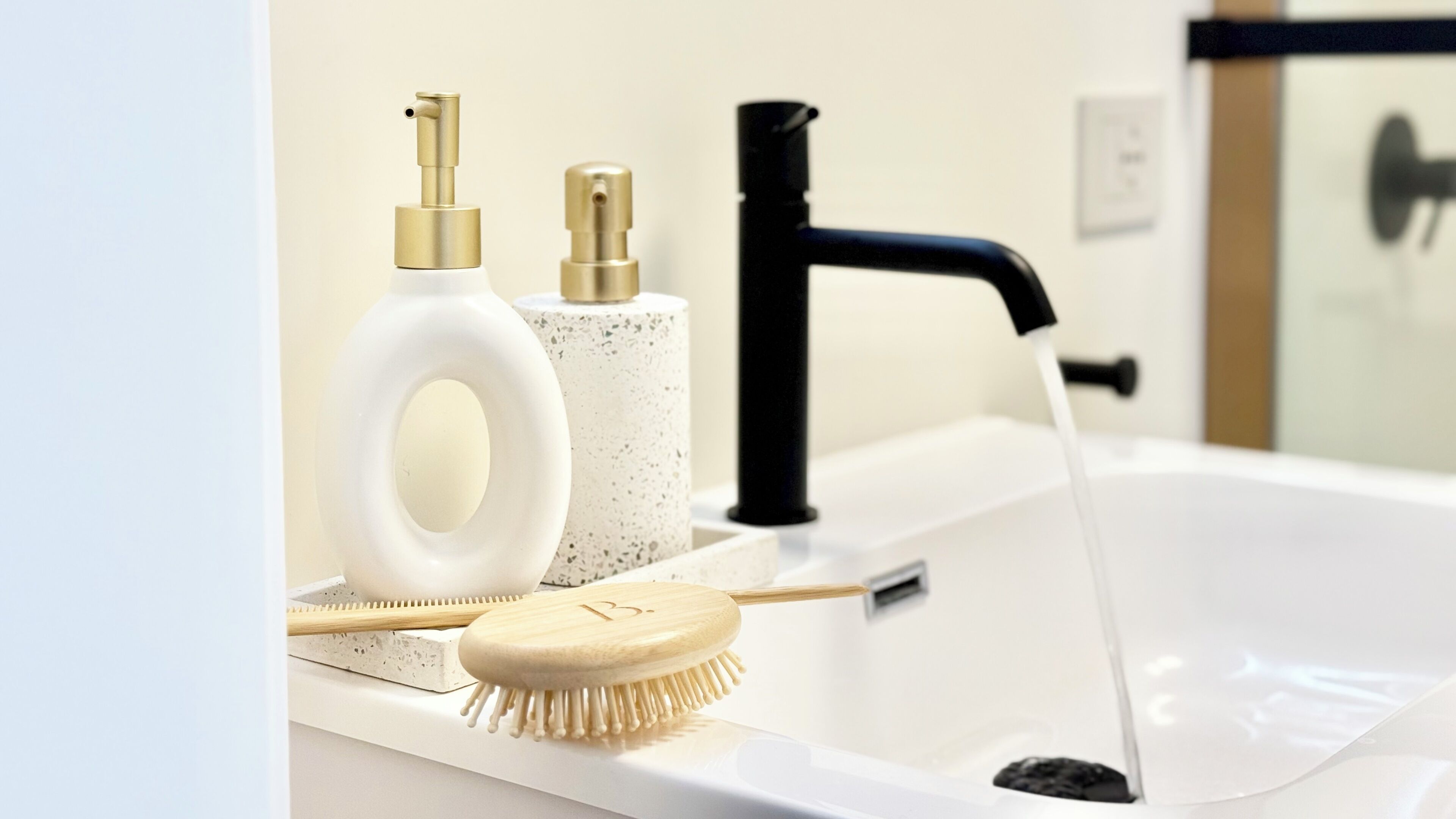 A bathroom sink with a black faucet, a white soap dispenser, and a wooden brush.