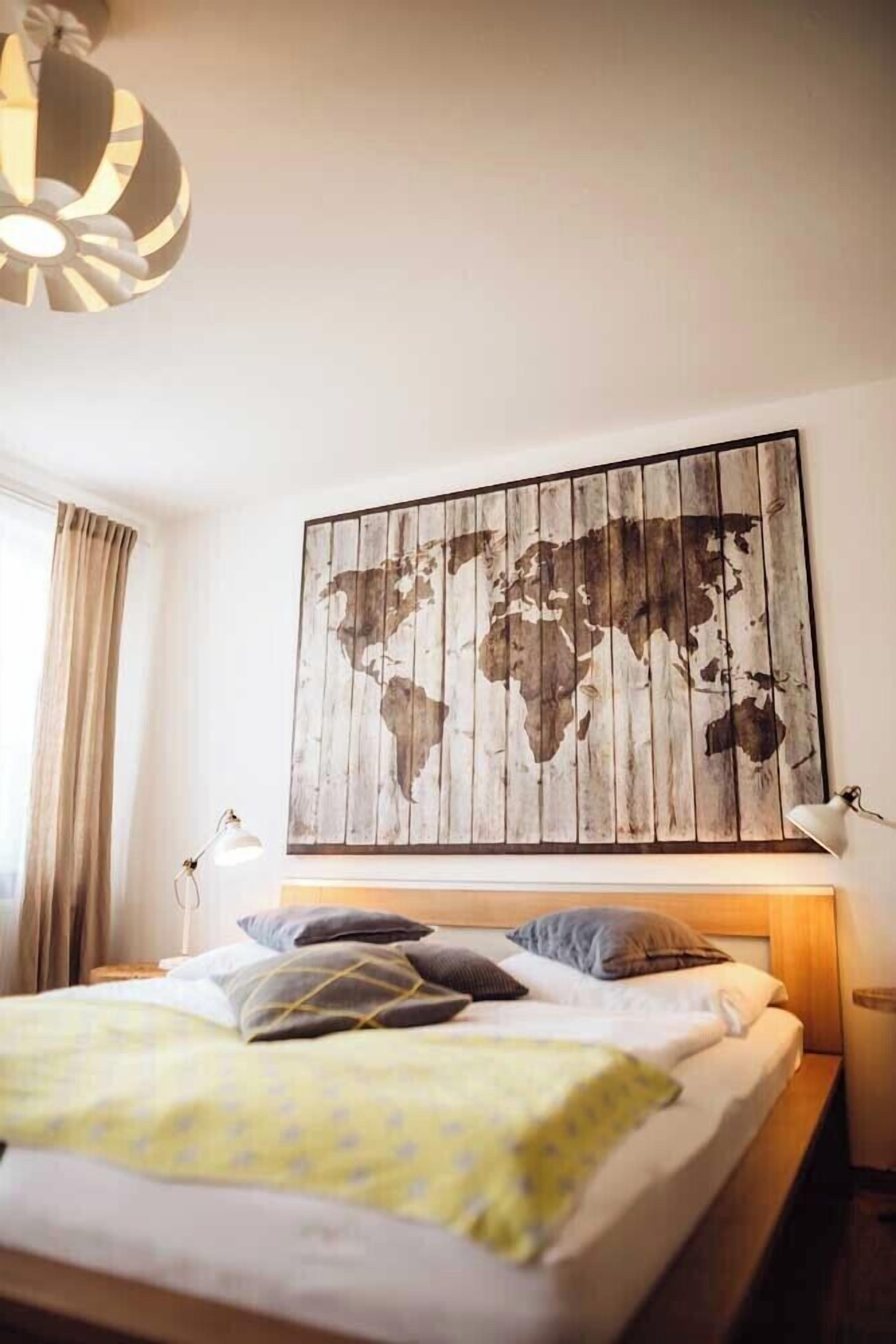A hotel room with a bed, a world map artwork on the wall, and a lamp on the nightstand.