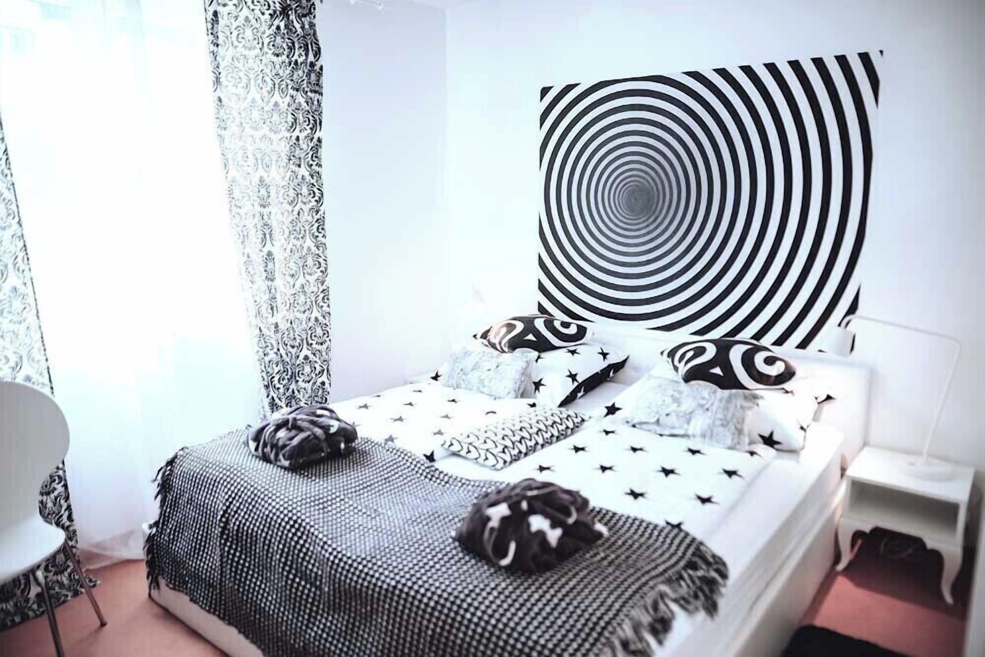 Een slaapkamer met een bed, kussens, een kunstwerk aan de muur en een raam met gordijnen.