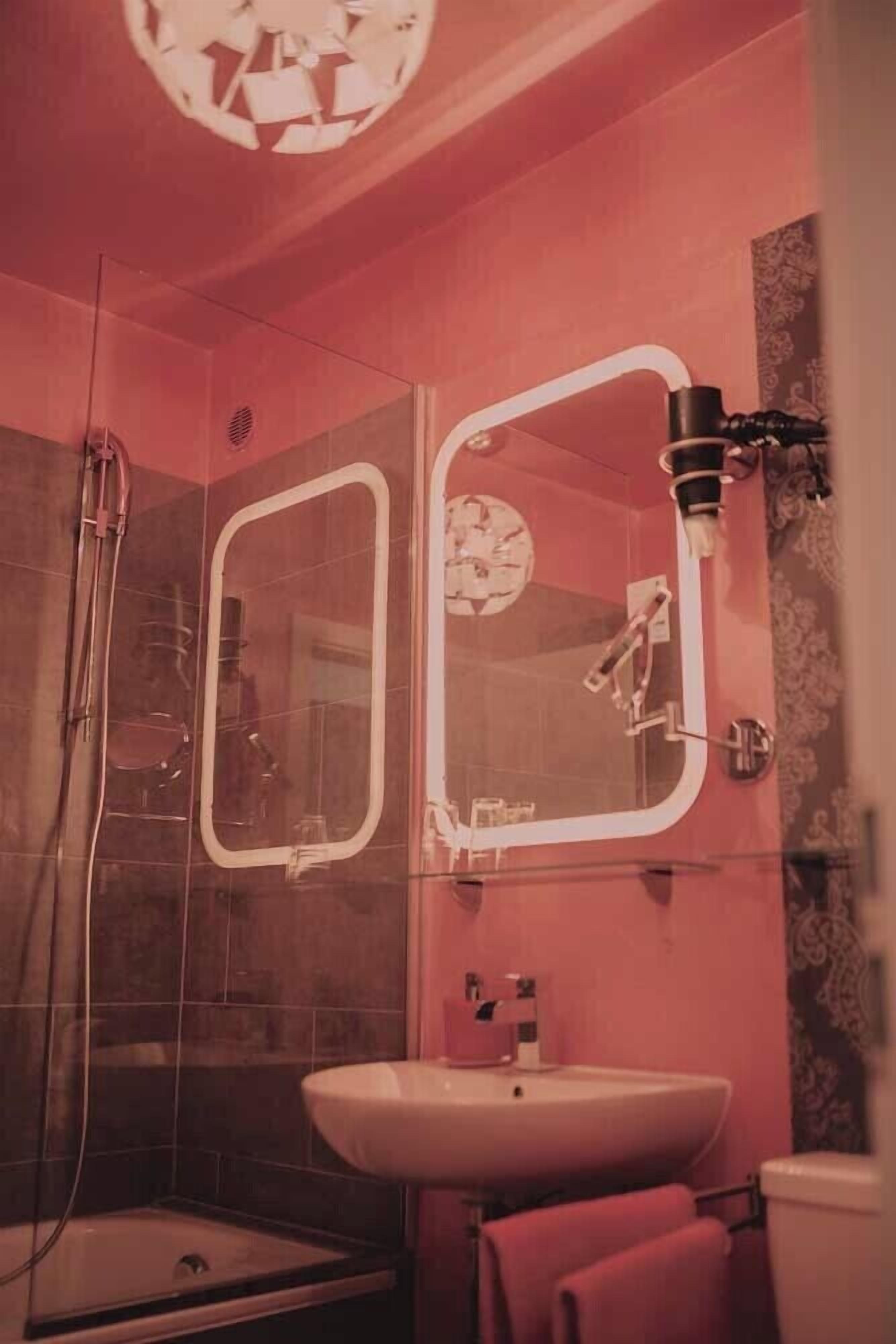 Un baño con ducha, lavamanos y dos espejos.