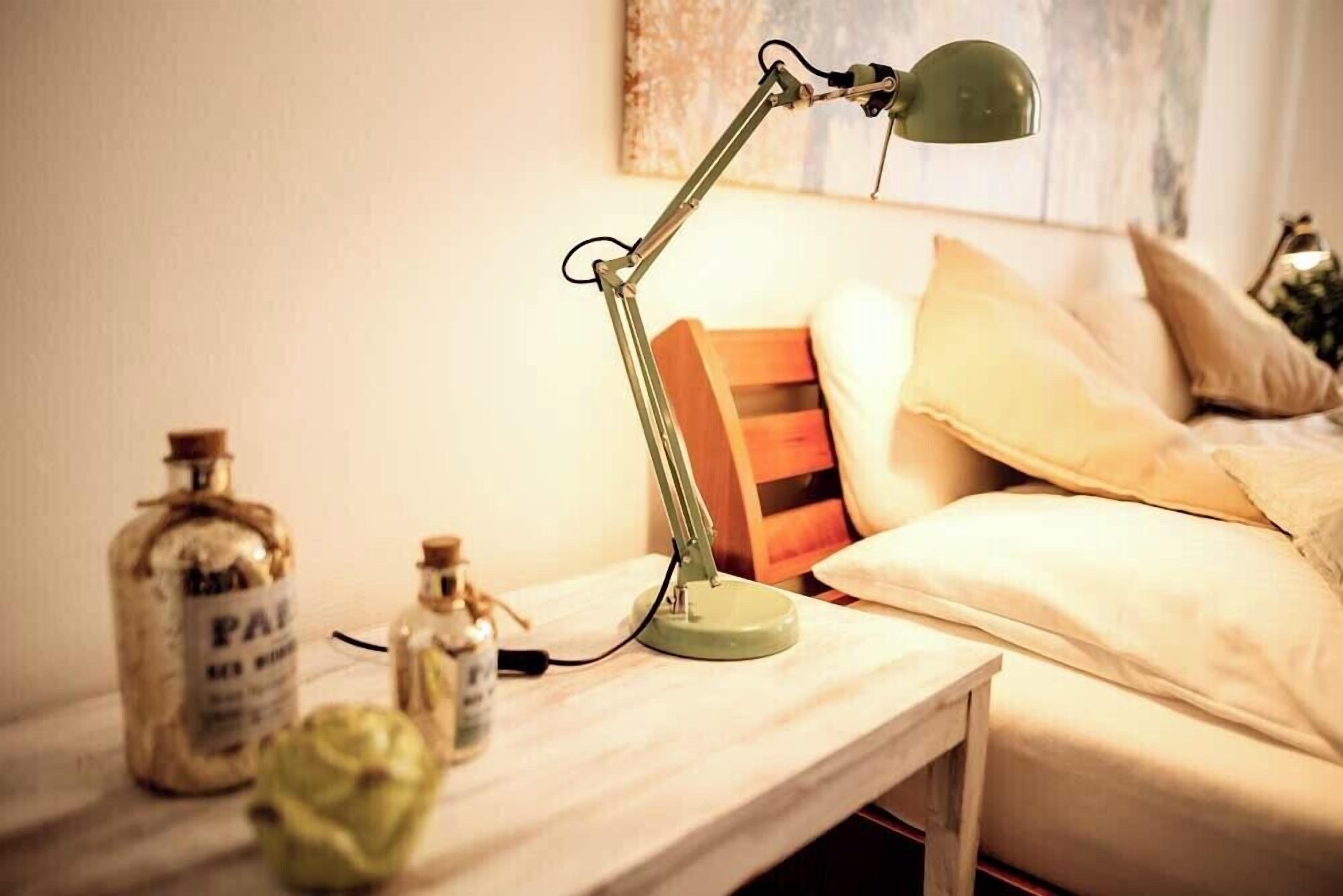 A bedside table with a lamp, a bottle, and a small vase.