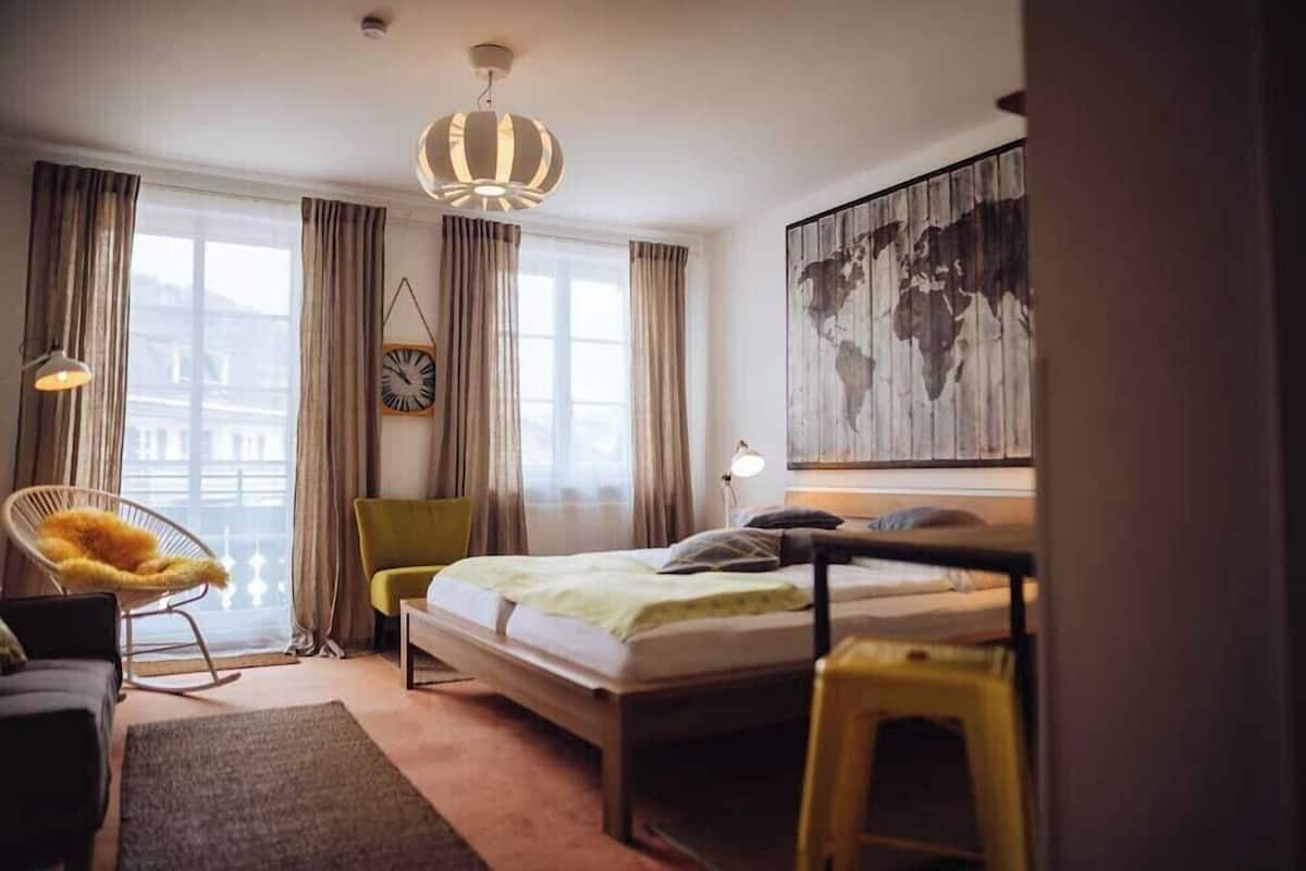 A modern hotel room with a bed, a chair, a desk, and a large world map on the wall.