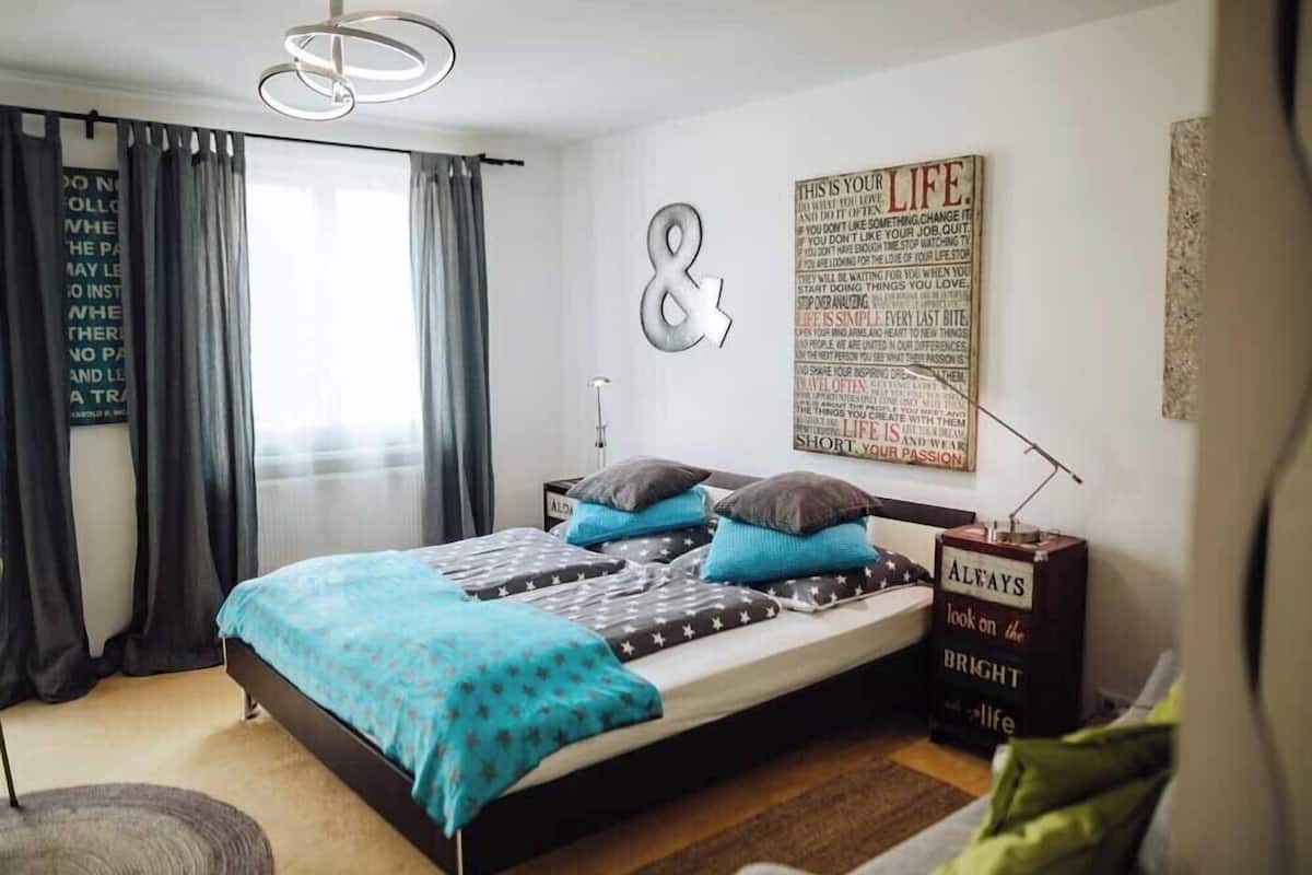 A modern bedroom with a bed, curtains, a wall-mounted light, and motivational posters.