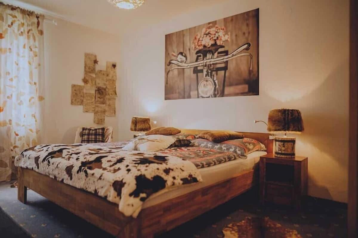 A bedroom with a wooden bed, a wall-mounted painting, and a nightstand with a lamp.