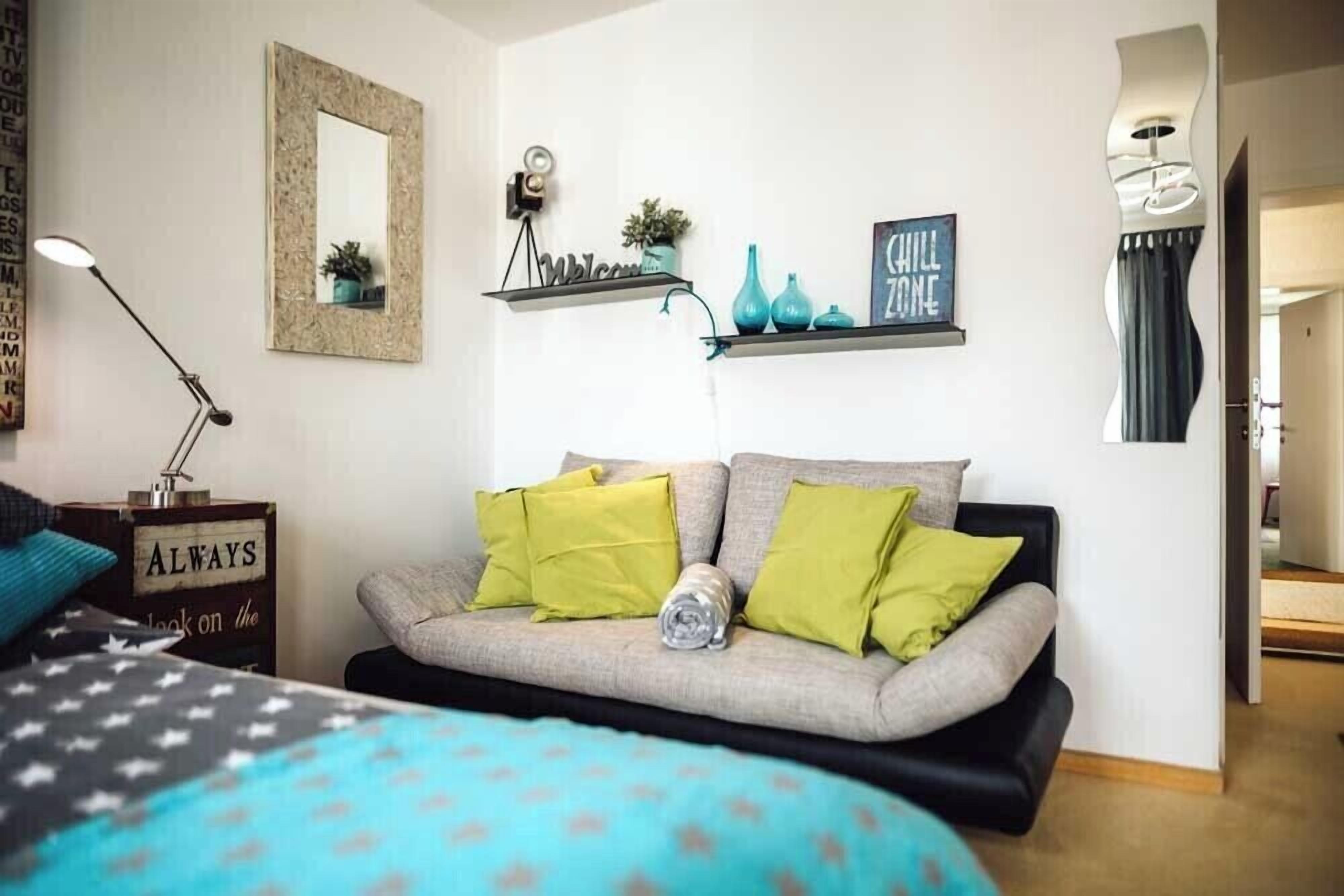 A modern bedroom with a bed, a sofa, a desk with a lamp, and a wall with decorative items.
