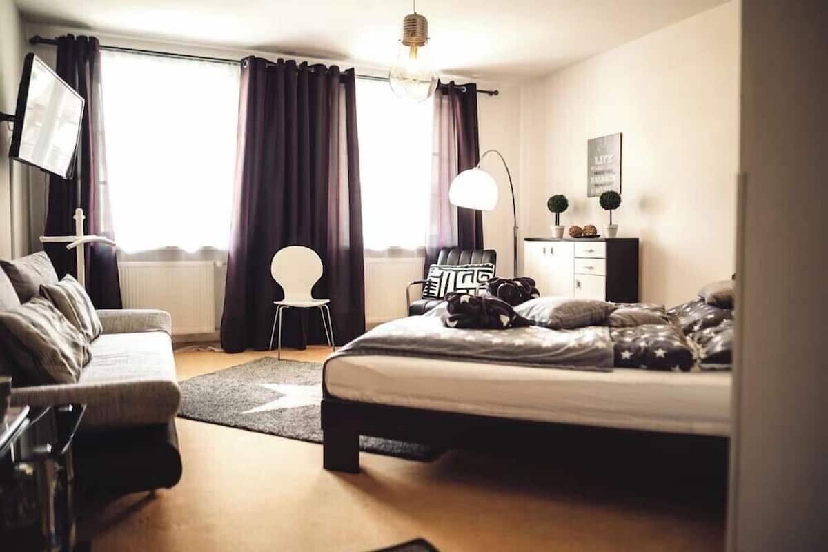 A modern bedroom with a bed, a desk, a chair, and a large window with curtains.