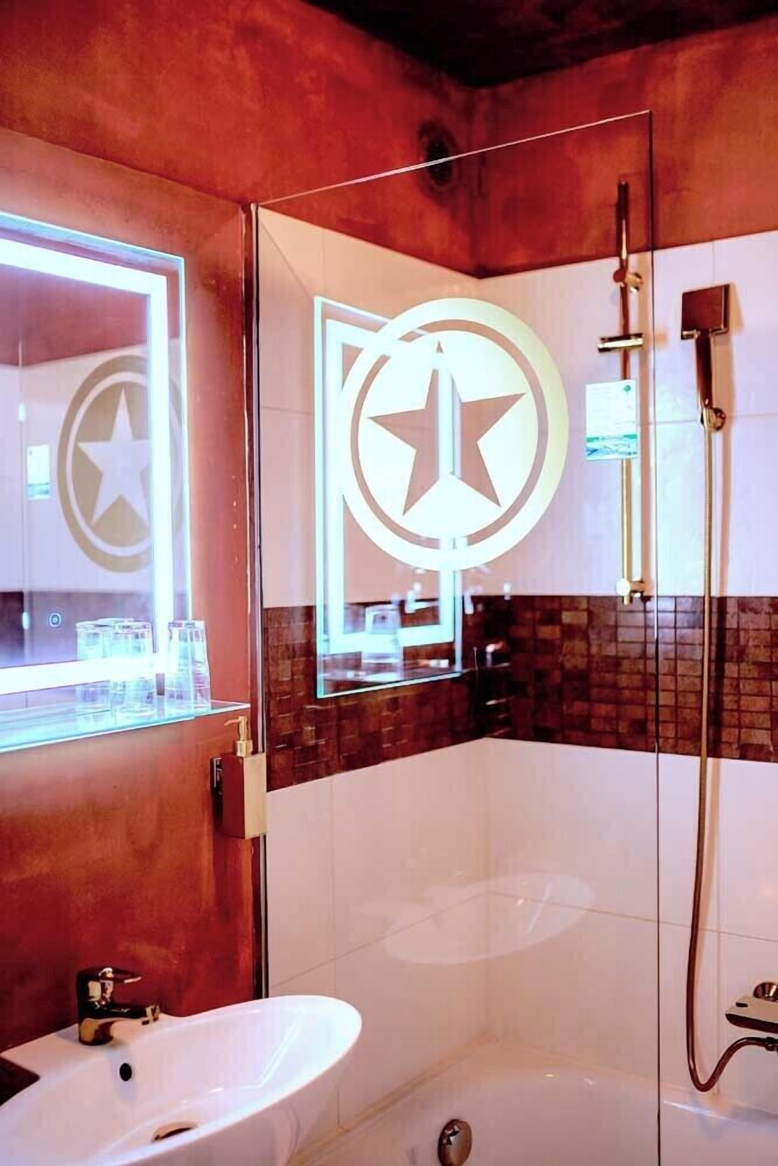 Une salle de bain moderne avec un grand miroir, un luminaire en forme d’étoile, une cabine de douche en verre et un lavabo blanc.