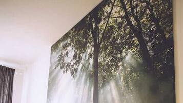 A bedroom with a bed, a bedside table, a lamp, and a large forest-themed painting on the wall.