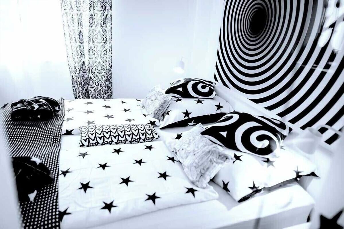 A neatly arranged bed with star-patterned bedding, a patterned pillow, and a rolled-up blanket.