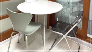 Une pièce d’angle avec une table ronde, deux chaises, une boîte de mouchoirs et une porte en verre décorée de motifs floraux.