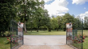 Una entrada porticada con un camino de grava que la atraviesa, rodeada de árboles y un cielo despejado.