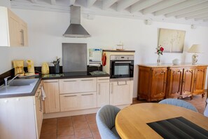 Une cuisine équipée d’une cuisinière, d’un four et de placards, une table à manger avec des chaises, et un meuble en bois avec des tiroirs.