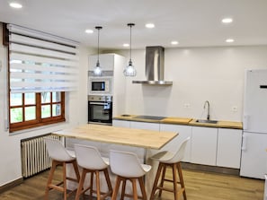 A modern kitchen with a central island, bar stools, a built-in oven, microwave, and stainless steel range hood. - Ländliches Anwesen "Mar y Montaña" (Meer und Berge) by Interhome (Lamuño)
