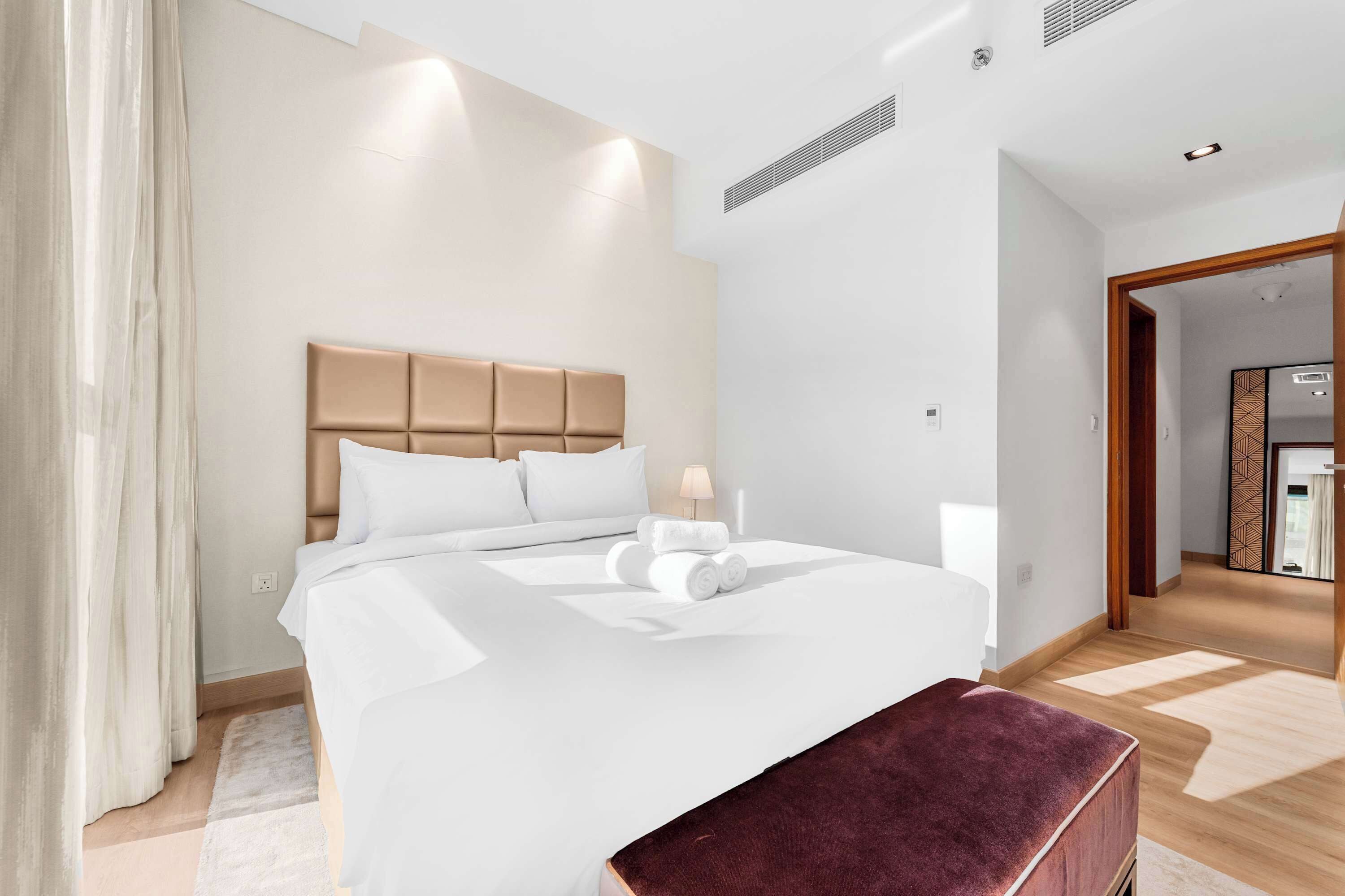 Una habitación de hotel moderna con una cama grande, cabecero de madera y un pequeño banco de madera.