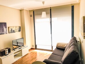 Ein Wohnzimmer mit einer Couch, einem Fernseher und einem Fenster mit Vorhängen.