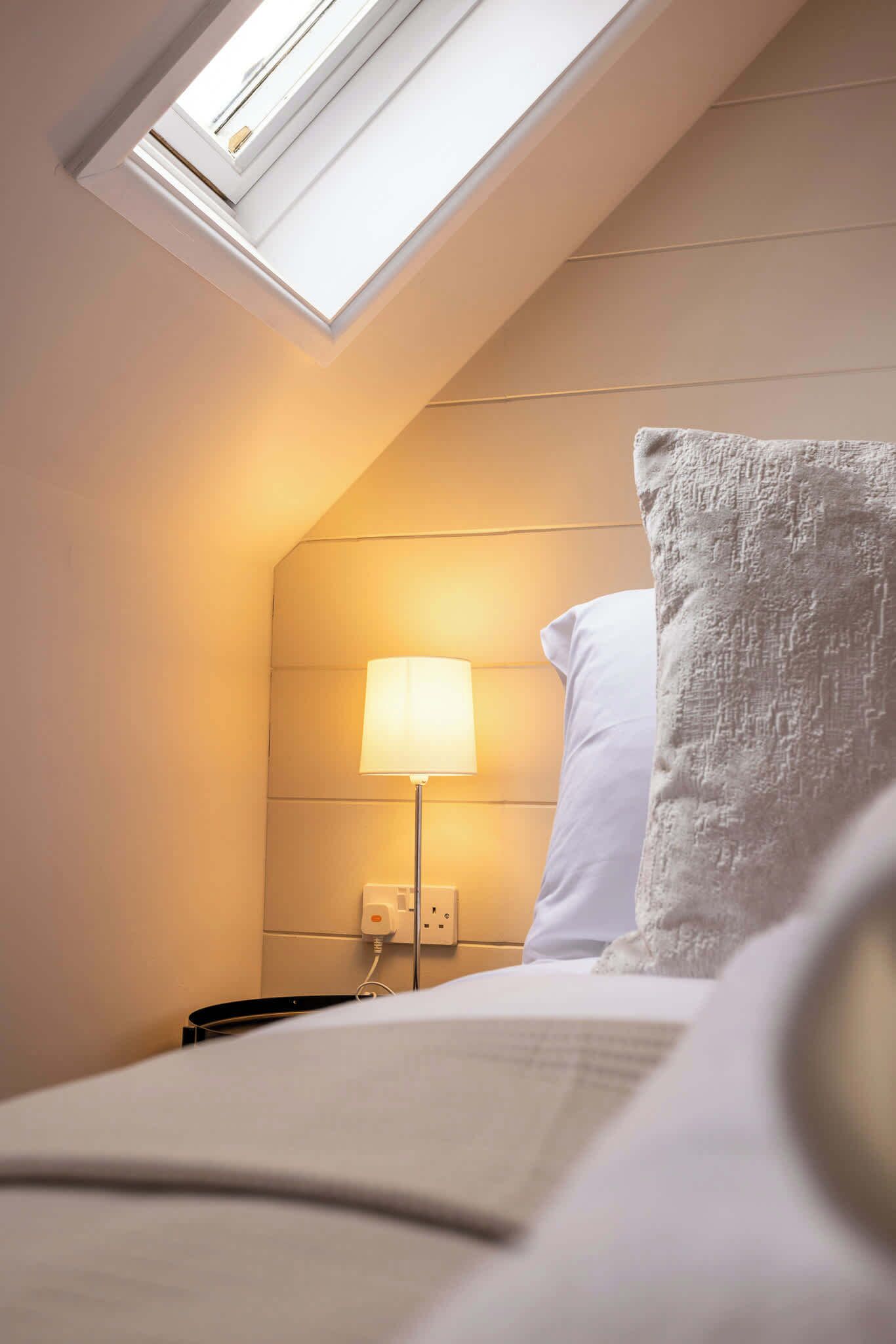 Une chambre d’hôtel avec une lucarne, une lampe de chevet, un oreiller et un lit.