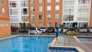 A swimming pool with a tiled deck, surrounded by a fence, and adjacent to a multi-story residential building with balconies. - South of Cali Quiet Modern (Cali)