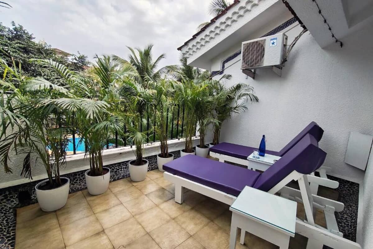 A rooftop terrace with two purple lounge chairs, a small table, and several potted plants.