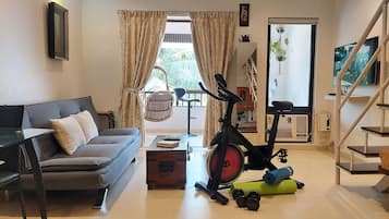 A living room with a sofa, a standing fan, exercise equipment, and a TV.
