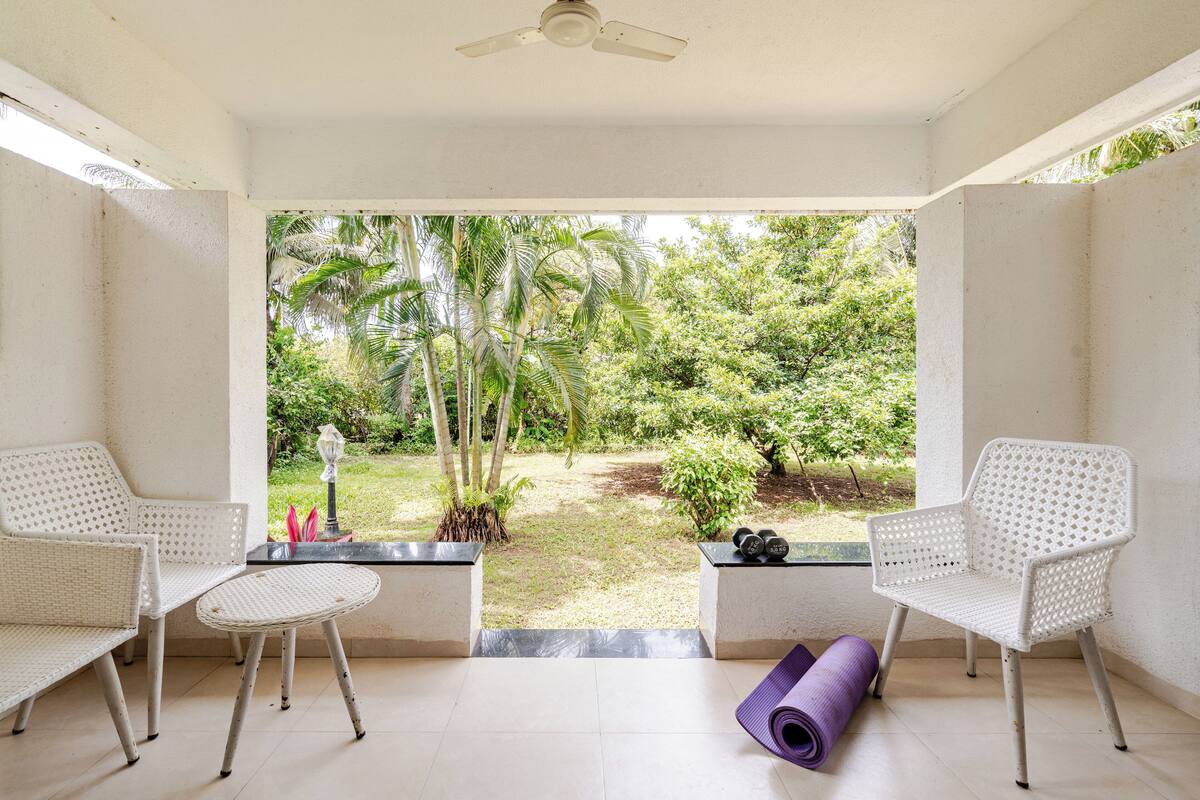 A room with two white wicker chairs, a small table, and a yoga mat.