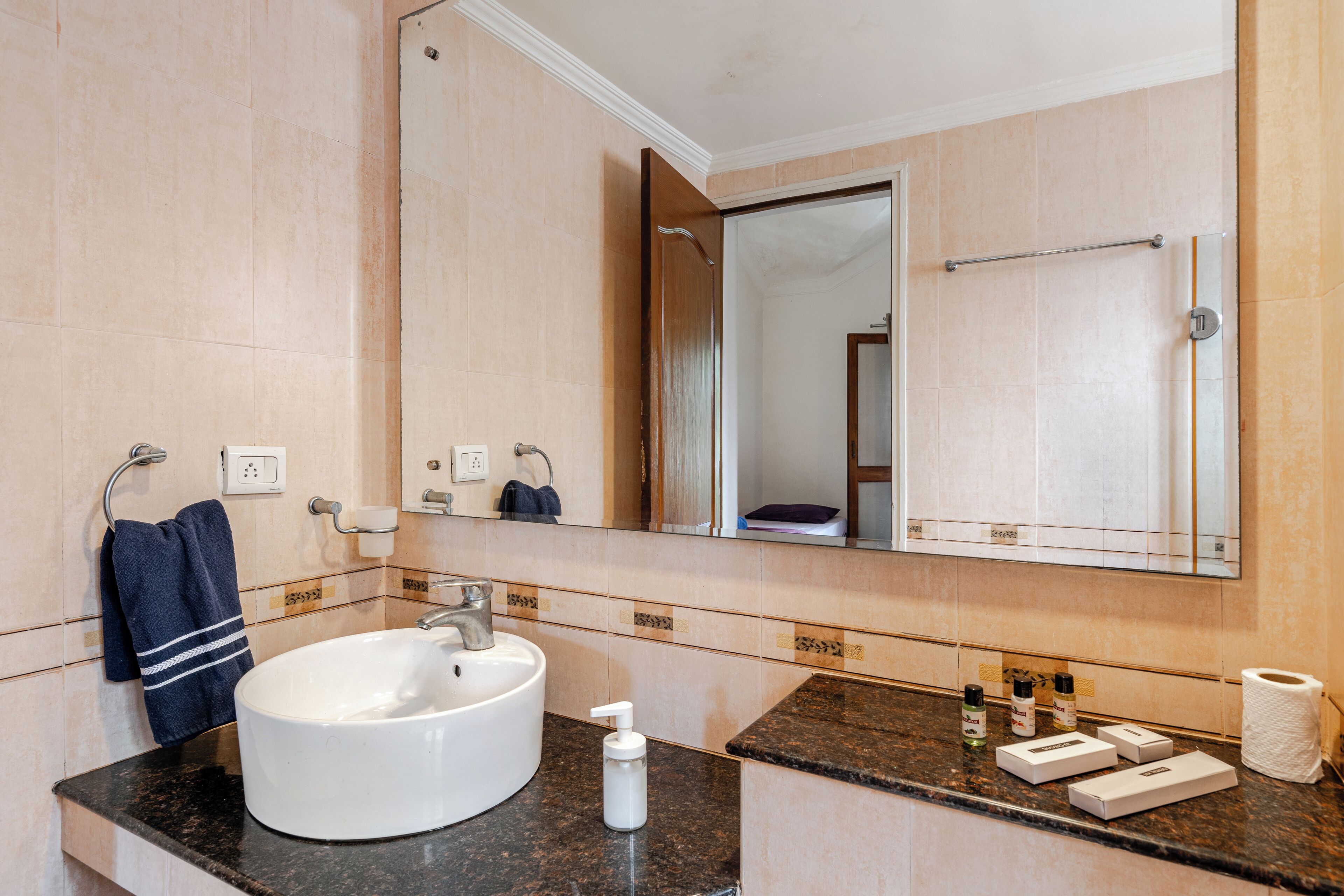 A bathroom with a round sink, a mirror, a towel rack, and toiletries on the counter.