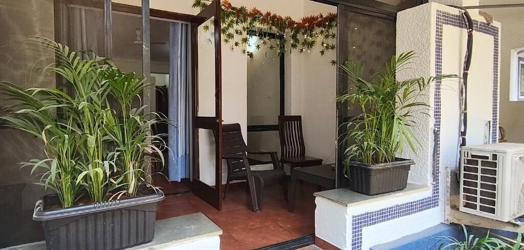 Une pièce dotée d’une porte-fenêtre coulissante, d’une petite table avec des chaises et de deux plantes en pot.