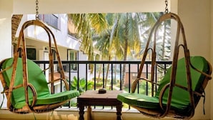 Een balkon met twee rieten stoelen en een kleine tafel, met uitzicht op een woongebied met palmbomen.