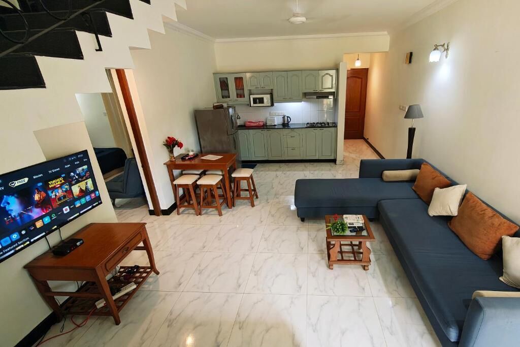 Een woonkamer met een televisie, bank, salontafel en een eetgedeelte met stoelen en een tafel.