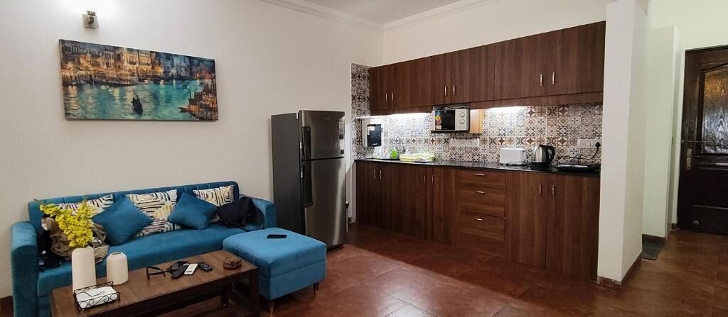A compact living space with a kitchenette, a sofa with cushions, and a painting on the wall.